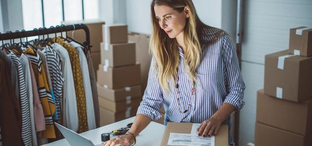 Woman scrolling on her computer while packaging a box